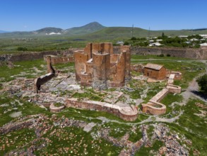 Ruins of an old brick fortress in the middle of a green landscape with mountains in the background,
