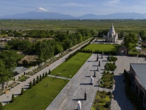 Spacious garden with statues and temple, surrounded by nature and mountains in the distance, aerial