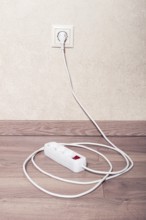 Electrical power strip connected to wall outlet on wooden floor in bright room