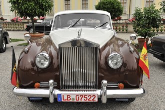 Brown vintage Rolls-Royce with flags parked in front of historic buildings, Retro Classics meets