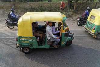 Yellow and green rickshaw with riders on a busy road, accompanied by motorcyclists, Agra, Jodhpur,