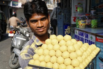 Udaipur, Rajasthan, North India, Asia, A vendor offers a platter full of traditional Indian laddus