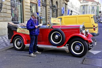 Prague, Czech Republic, Europe, Man reading in front of a classic red vintage car on a busy street