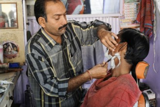 Kota, Rajasthan, North India, Asia, A barber shaves a customer's face in a small hairdressing