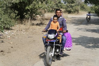 Kota, Rajasthan, North India, Asia, Family riding a motorbike along a rural road in sunny weather,