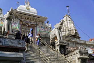 Entrance to Jagdish Temple, Udaipur, people climb the steps to a temple flanked by statues under a