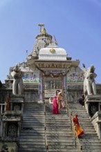 Entrance to Jagdish Temple, Udaipur, people climb the steps to a temple flanked by statues under a