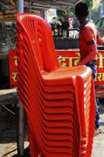 Udaipur, Rajasthan, North India, India, Asia, Stacked red plastic chairs in a lively market with