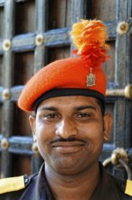 Udaipur, Rajasthan, North India, Asia, A man in uniform with an orange cap and feather smiles in