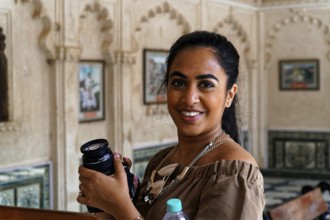 Smiling woman holding a camera lens in a decorative interior, Udaipur, Rajasthan, North India