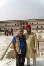 Red Fort, Agra, Uttar Pradesh, India, Two men smile warmly against a historic backdrop while groups