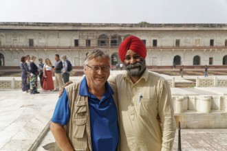 Red Fort, Agra, Uttar Pradesh, India, Two men smile friendly in the historic courtyard while groups