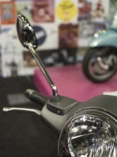 Mirror of a retro scooter in the foreground with colourful posters in the blurred background,
