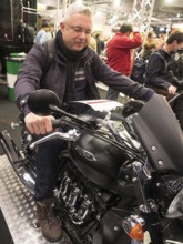 Man sitting on a Triumph motorbike, surrounded by trade fair visitors, dortmund, deutchland