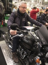 Person sitting on a black motorbike in the middle of a busy exhibition, dortmund, deutchland