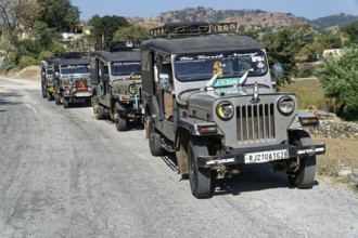 A convoy of jeeps drives along a country road in a mountainous region, Ranakpur, Jodhpur,