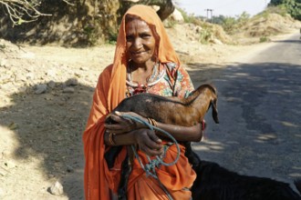 Elderly woman in traditional dress holding a goat in a rural area, Ranakpur, Jodhpur, Rajasthan,