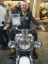 Smiling man sitting on a motorbike during a trade fair and enjoying himself, dortmund, germany