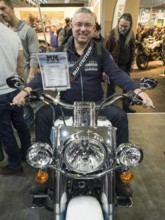 Smiling man sitting on a motorbike during a trade fair and enjoying himself, dortmund, germany