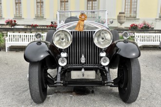 Black classic vintage car with red ribbon, elegant in front of flower bed, Retro Classics meets