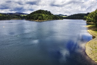 A calm lake (Aggertalsperre) with a wooded island, cloudy sky and reflecting water, Bergneustadt