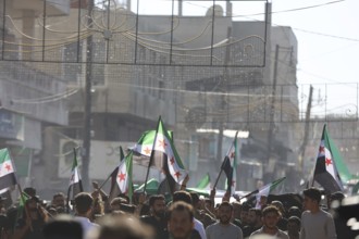 Thousands of Syrians march in Idlib carrying the Syrian revolutionary flag during a protest against