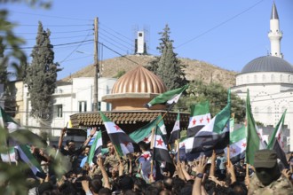 Thousands of Syrians march in Idlib carrying the Syrian revolutionary flag during a protest against