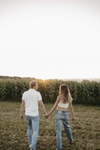 Couple walking hand in hand across a mown field