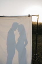 Pregnant young woman with partner in silhouette behind a sheet