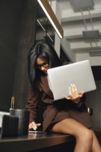 A woman with glasses is focused on tasks as she sits at a contemporary office desk. She holds a