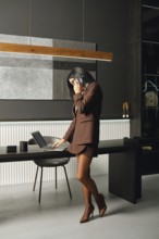 A businesswoman stands in a modern office space, engaged in a phone conversation while reviewing
