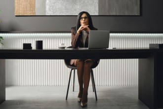 A woman in business attire sits at a sleek desk, hands clasped and focused. She is focused on