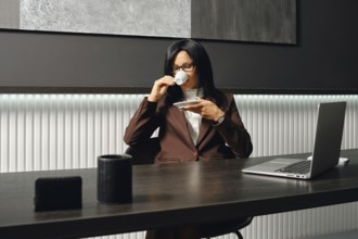 A real estate agent in a brown suit sits at a desk, sipping coffee from a small cup in a