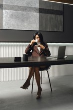 A confident businesswoman is seated at a sleek desk in a contemporary office. She sips coffee while