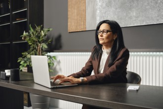 A businesswoman sits at a desk and typing on her laptop in an office. The space features elegant