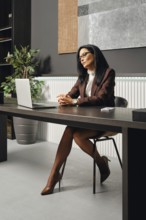 A woman dressed in business attire sits at an office desk in office and looking at the screen of