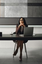 A businesswoman sits at a sleek desk in a contemporary office, dressed in strict suit. She gazes