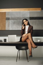 A confident businesswoman with slender legs in high hells sits on a tabletop of an office desk,