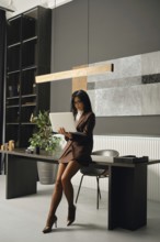 A focused woman sits at an elegant desk in a contemporary office space, utilising her laptop which