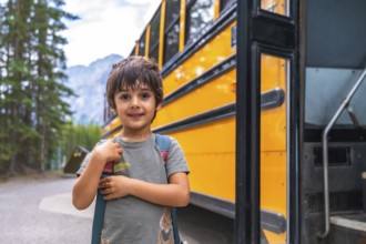 Happy elementary school student carrying backpack is waiting for the school bus in a mountain