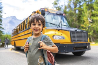 Happy schoolboy carrying backpack is waiting for the school bus in front of blurred mountain