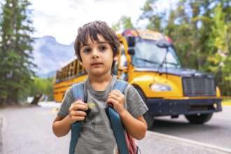 Elementary school student carrying backpack standing on a mountain road waiting for the school bus
