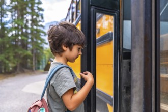 Curious preschool student with a backpack examines a yellow school bus before boarding, showing the