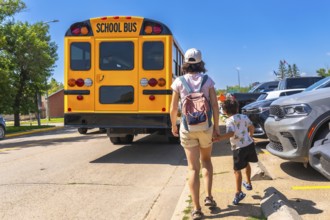 Mother walking her son to the school bus on the first day back to school, holding hands and heading