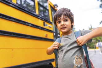 Elementary school student wearing a backpack, waiting for the bus on a bright, sunny day, excitedly