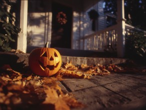 A carved pumpkin with a smiling face stands on a house wall in front of a residential building,