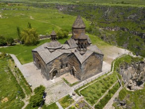 Medieval stone church with a surrounding green landscape and cliffs, aerial view, Saghmosavank