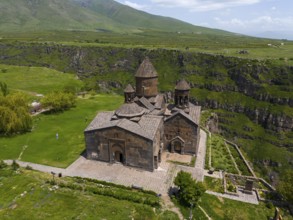 Historic stone church on a green plain in front of a mountain landscape under a blue sky, aerial