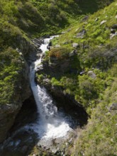 Waterfall between rocks and green vegetation in a mountain landscape, aerial view, waterfall near