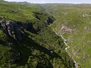 A deep gorge with a river surrounded by green hills under a clear blue sky, aerial view, river and